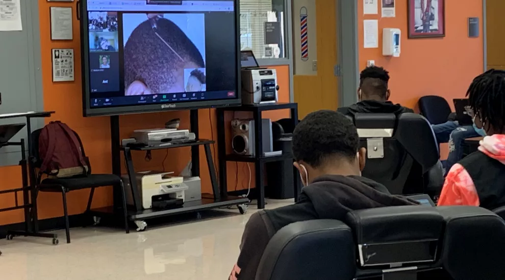 Students practice barbering techniques using online computer software 