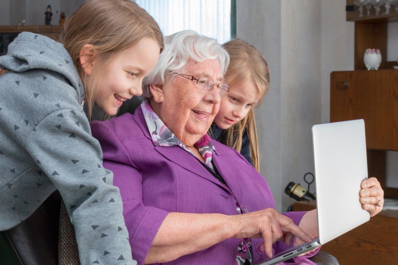 photo of grandmother with two young granddaughters looking at a laptop screen together