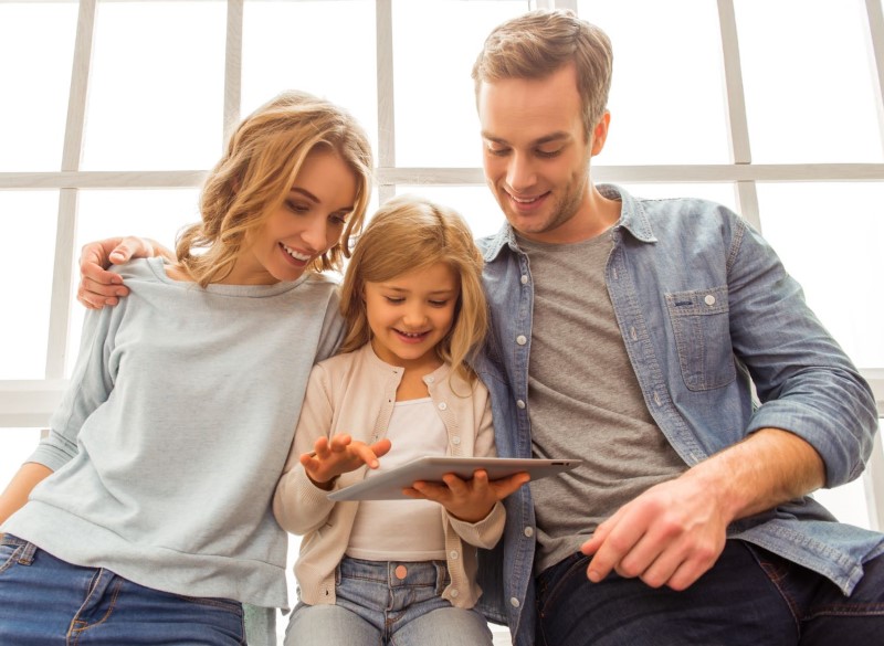 photo of mother and father looking at a tablet screen with their daughter