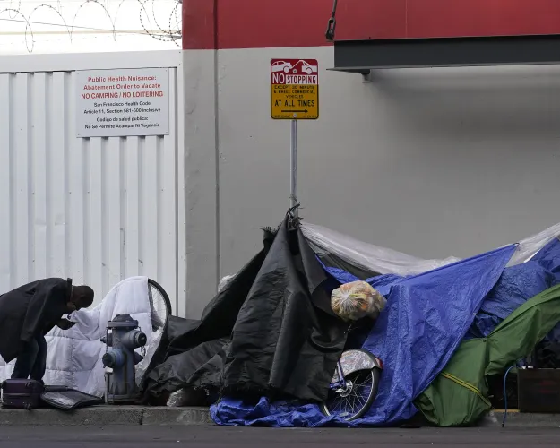 FILE - A man stands near tents on a sidewalk in San Francisco, Nov. 21, 2020.