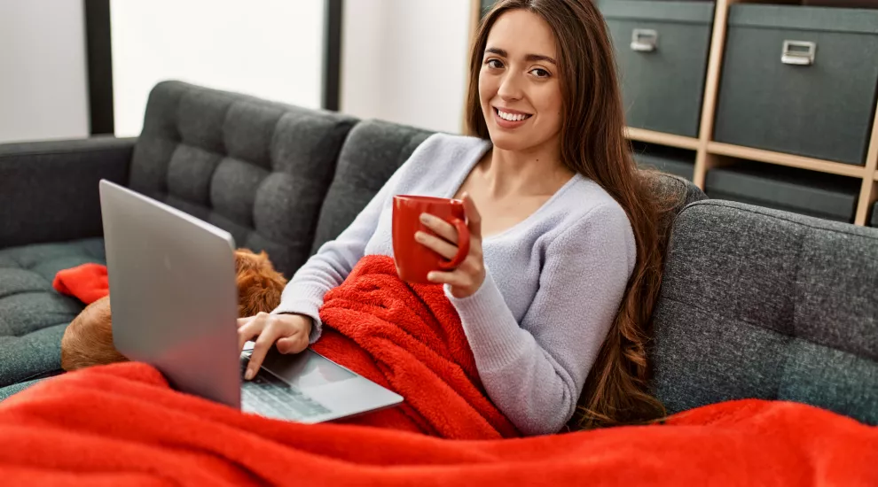 Woman on sofa with blanket and laptop