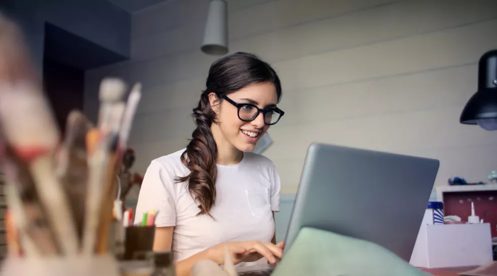 photo of a woman sitting at a desk, using a laptop and smiling