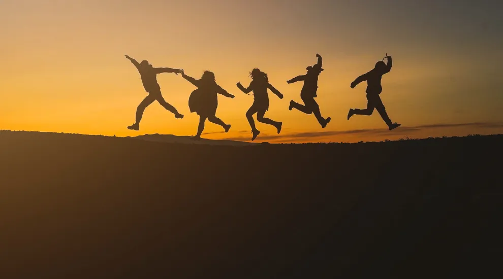 photo of 5 people leaping in the air against sky silhouette