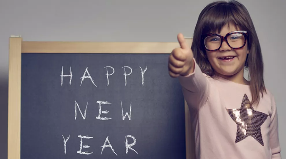 Girl smiling by blackboard that has "Happy New Year's" written on it