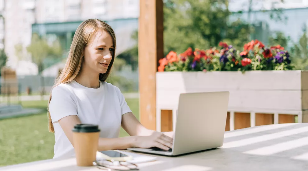 photo of woman using a laptop outside at a table with flowers