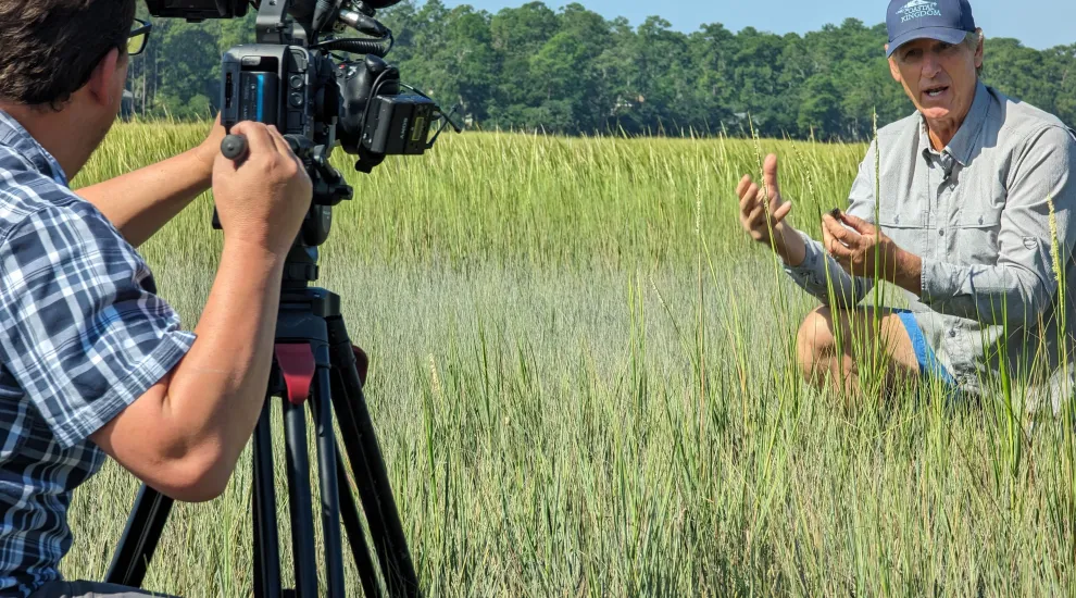 Tony Mills hold up an animal while filming in the salt marsh