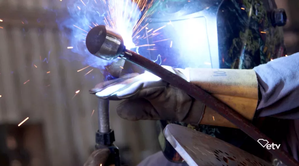 Photograph of a gloved hand welding a piece of steel with sparks flying.