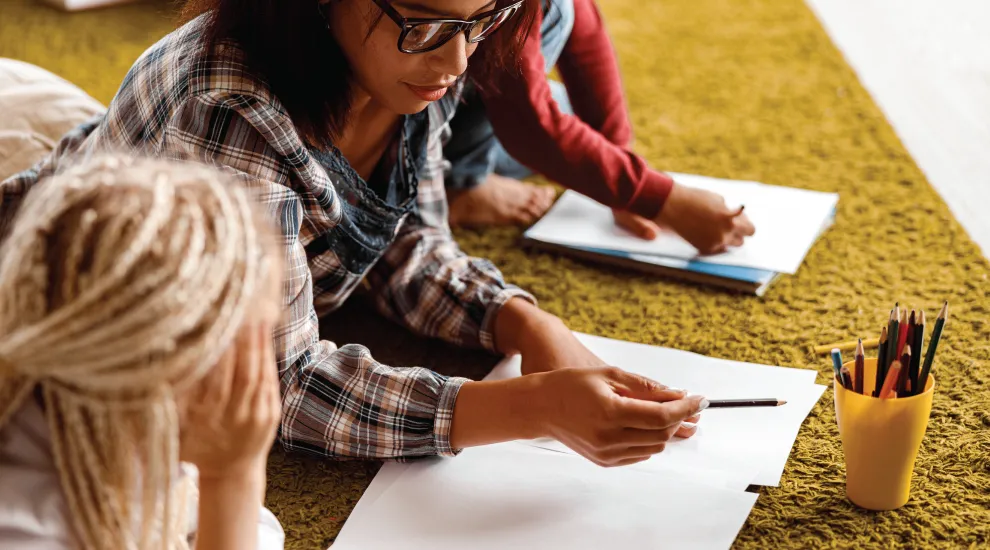 photo of adult on floor leading drawing activity with two children