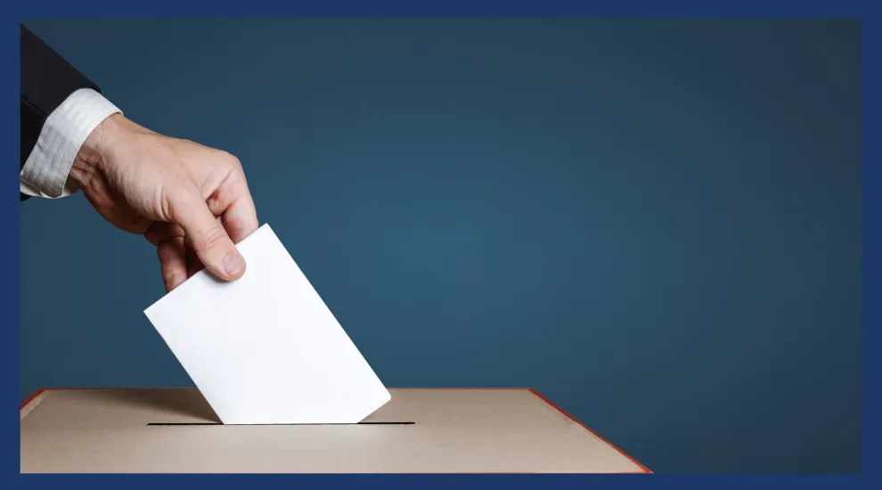 A hand placing a ballot in a box