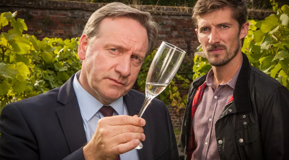 Man holding glass of champaign as other man looks on