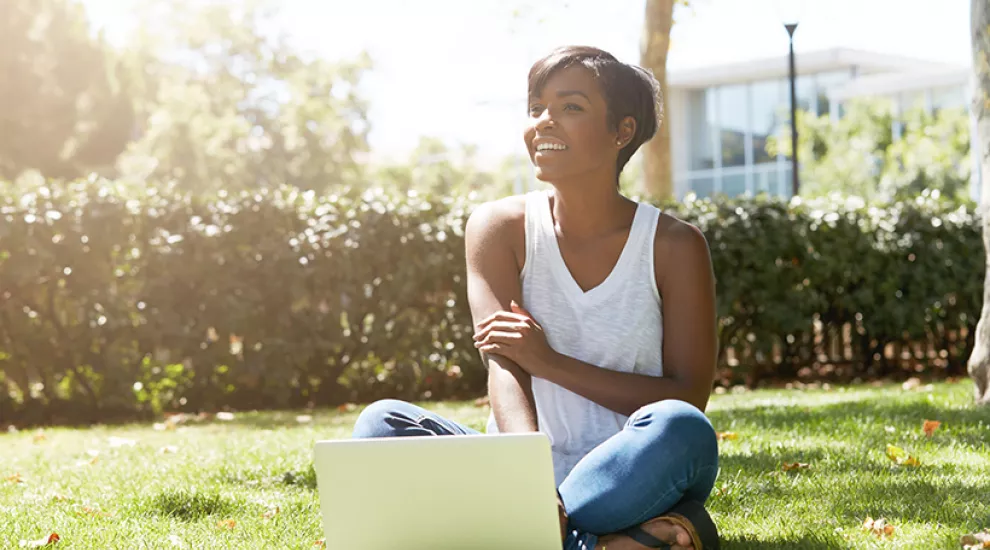 Black woman smiling working at laptop outside