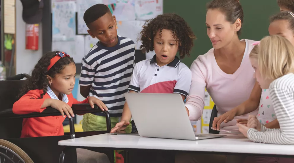 photo of teacher and students looking at a laptop screen together