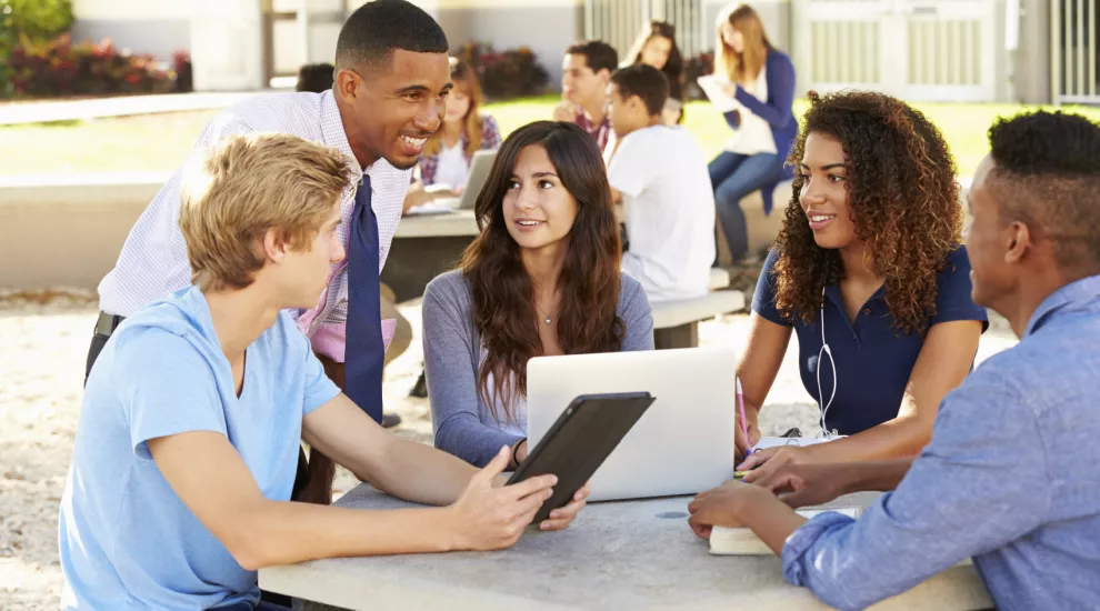 High school students sitting around a table with a tablet with teacher engaging with them