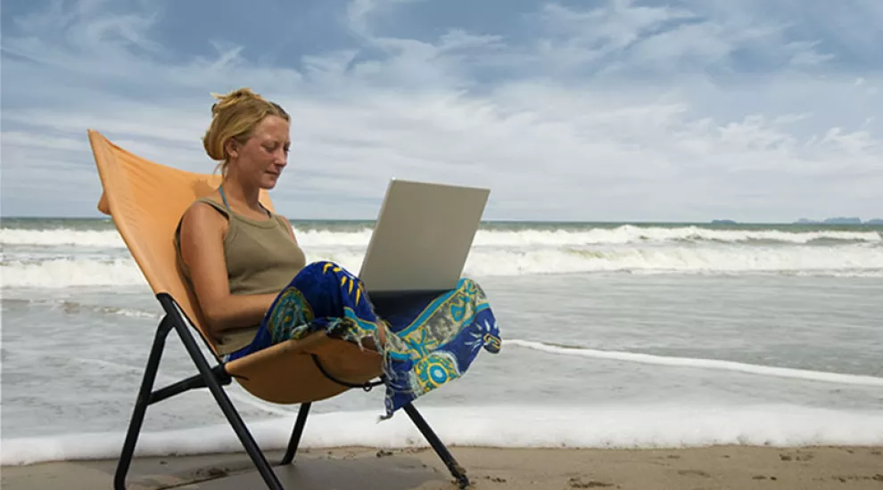 Teacher sitting on beach with laptop