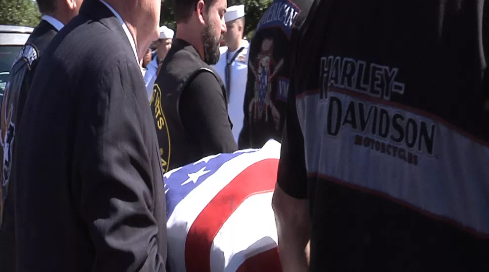 Pallbearers carry a casket with an American flag draped over it
