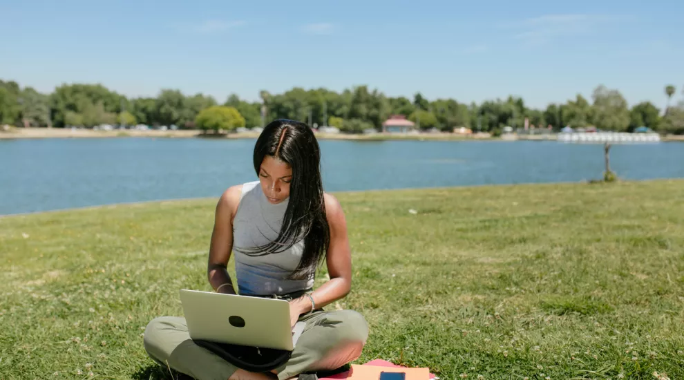 woman sitting outside by a lake using a laptop