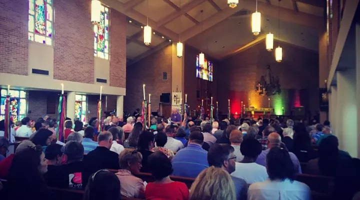 Congregation sits at vigil, altar lit in rainbow colors
