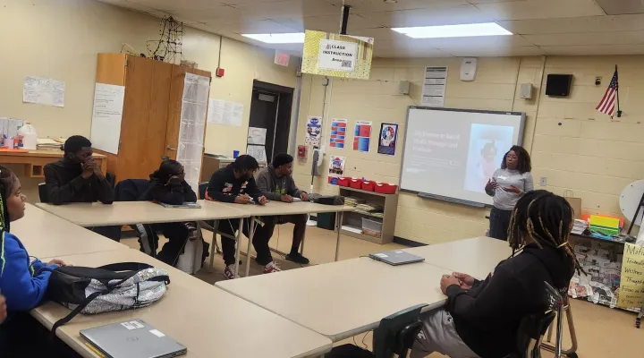 photo of woman giving presentation to several seated high-school students in a classroom