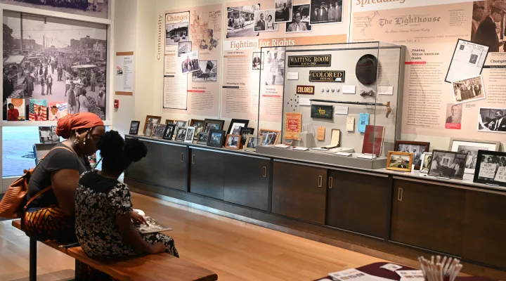photo of a woman and student sitting on a bench in a museum setting viewing materials from a Civil Rights display