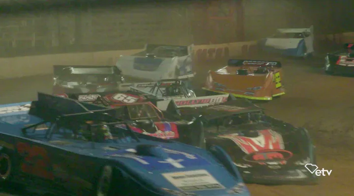 Photograph of dirt track race cars at night drifting around a turn on the racetrack.