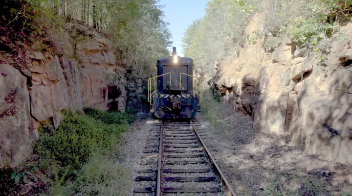 Photo showing the front of a locomotive engine while underway and passing through a narrow canyon