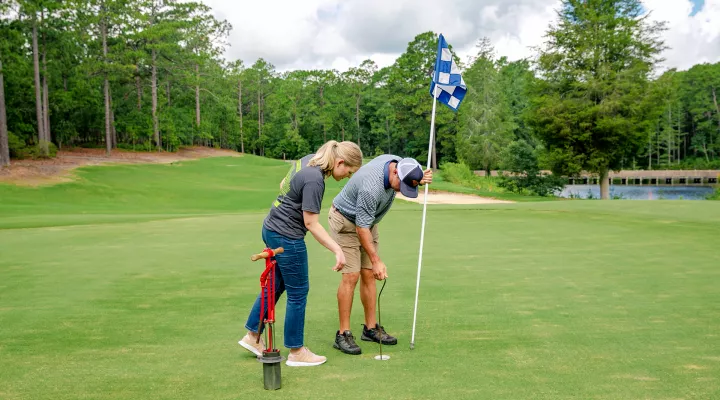 A man and a woman inspect a hole on a golf course.