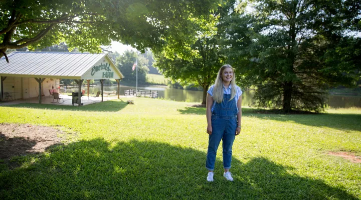 Devyn stands smiling in a large grassy area in front of the Emerald Farm building.