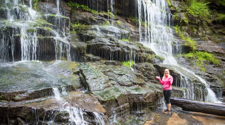 Devyn stands smiling in front of a waterfall.