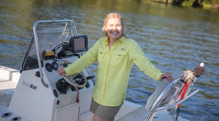 Devyn stands smiling at the wheel of a small fishing boat.