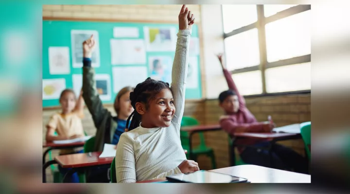 Kids with hands raised at desks in classroom