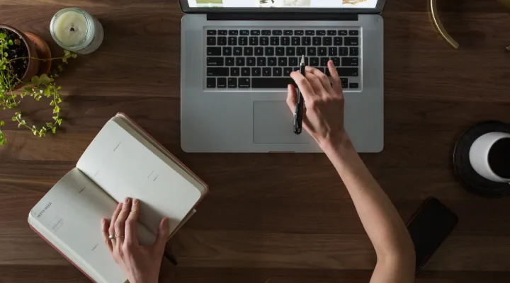 photo of person with hand on laptop and a planner