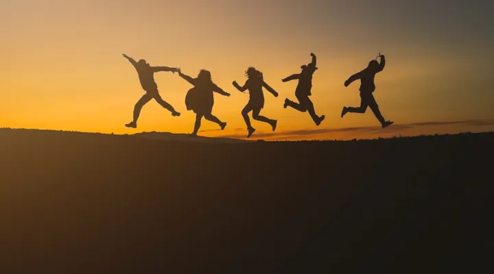 photo of 5 people leaping in the air against sky silhouette