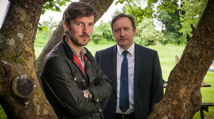 Two men standing by a tree.