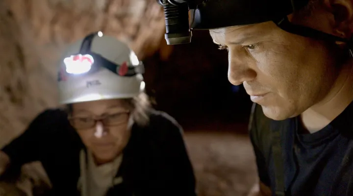 Man and woman inside cave, both wearing helmets with flashlights