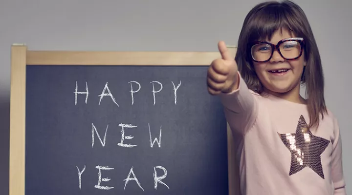 Girl smiling by blackboard that has "Happy New Year's" written on it