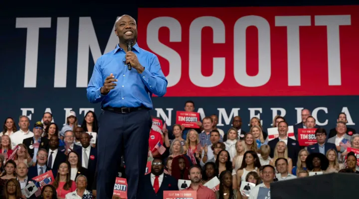 Senator Scott wearing a blue button down shirt and black trousers stands on stage during a campaign rally.