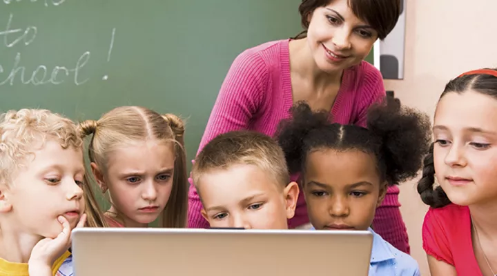 Teacher with young students viewing computer screen