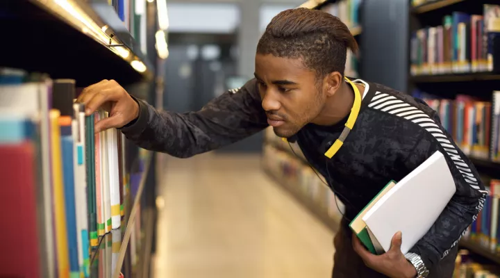 male teen student reaching for a book off library shelf