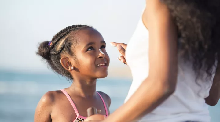 girl receiving sunscreen from mother