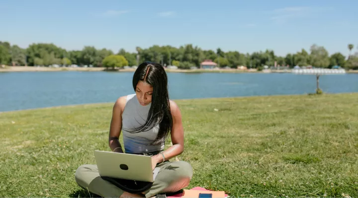 woman sitting outside by a lake using a laptop