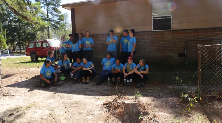 Teenagers in blue shirts laugh together while standing against a wall