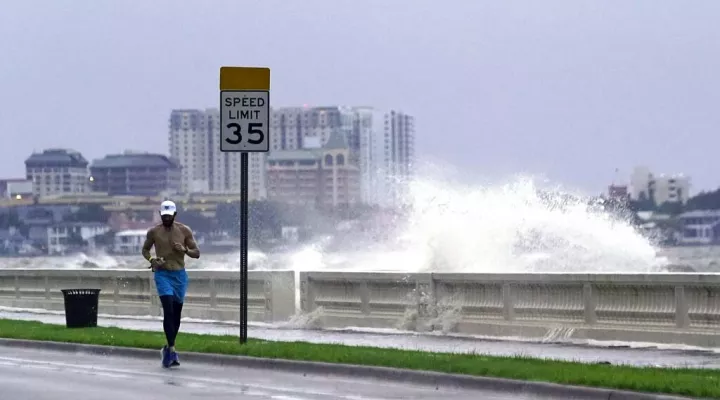 A jogger makes his way along Bayshore Blvd., in Tampa, Fla. as a wave breaks over a seawall, during the aftermath of Tropical Storm Elsa Wednesday, July 7, 2021. The Tampa Bay area was spared major damage as Elsa stayed off shore as it passed by. (AP Photo/John Raoux)