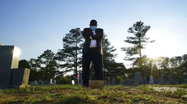 Mortician Shawn Troy stands at the grave of his father, William Penn Troy Sr., at Hillcrest Cemetery outside Mullins, S.C., on Sunday, May 23, 2021. The elder Troy, who developed the cemetery, died of COVID-19 in August 2020, one of many Black funeral directors to succumb during the pandemic. “I don’t think I’ll ever get over it,” he said. “But I’ll get through it.” (AP Photo/Allen G. Breed)