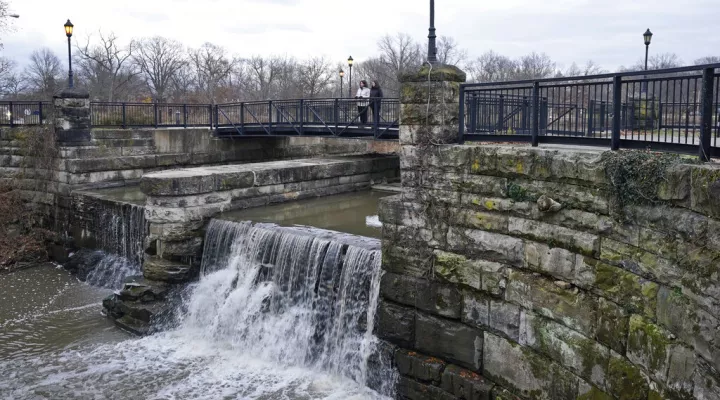 Two women look over the edge of Lower Shaker Lake Dam, Tuesday, Dec. 7, 2021, in Cleveland Heights, Ohio. In 2021, the cities of Cleveland Heights and Shaker Heights approved a $28.3 million plan to remove Horseshoe Lake Dam, return the area to a free-flowing stream and rebuild Lower Shaker Lake Dam. (AP Photo/Tony Dejak)