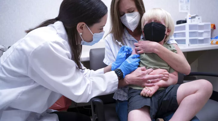 Pharmacist Kaitlin Harring, left, administers a Moderna COVID-19 vaccination to three year-old Fletcher Pack, while he sits on the lap of his mother, McKenzie Pack, at Walgreens pharmacy Monday, June 20, 2022, in Lexington, S.C. Today marked the first day COVID-19 vaccinations were made available to children under 5 in the United States. (AP Photo/Sean Rayford)