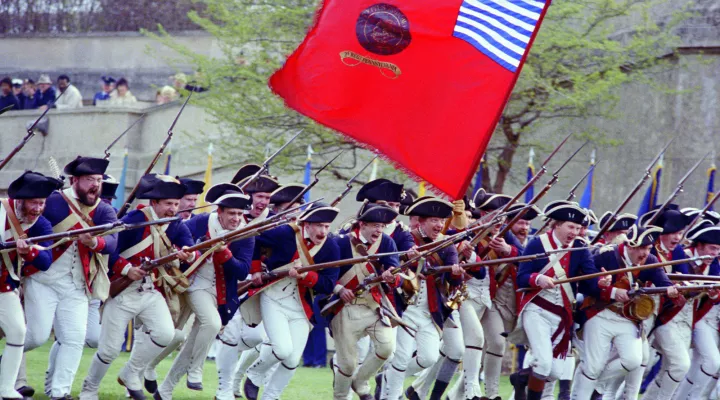 Troops wearing the Revolutionary War uniforms of the 9th Virginia Regiment, Corps of the Continental Line, participate in a drill and firing demonstration during the Cessation of Hostilities Bicentennial Celebration at the Pentagon River Plaza.  The flag of the ceremonial 2nd Pennsylvania Regiment, Corps of the Continental Line, is carried in the background.