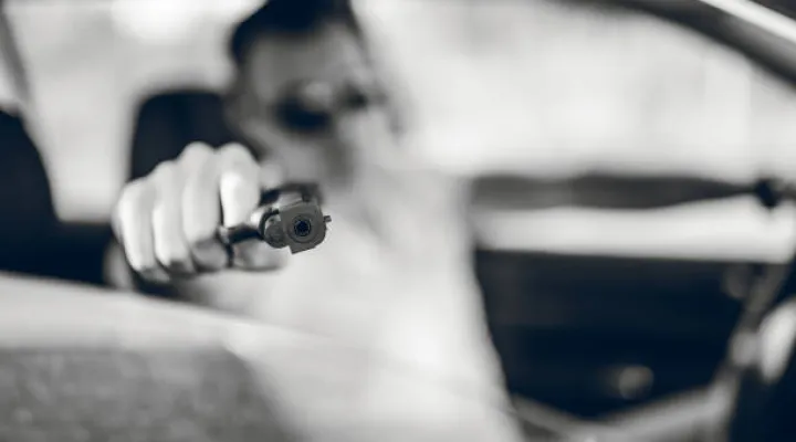 Man driving a car and holding a gun. Black and white.