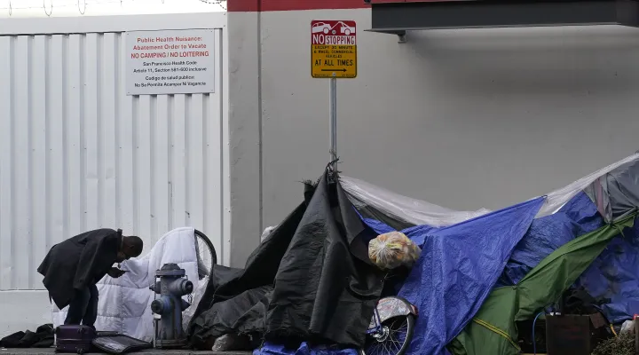 FILE - A man stands near tents on a sidewalk in San Francisco, Nov. 21, 2020.
